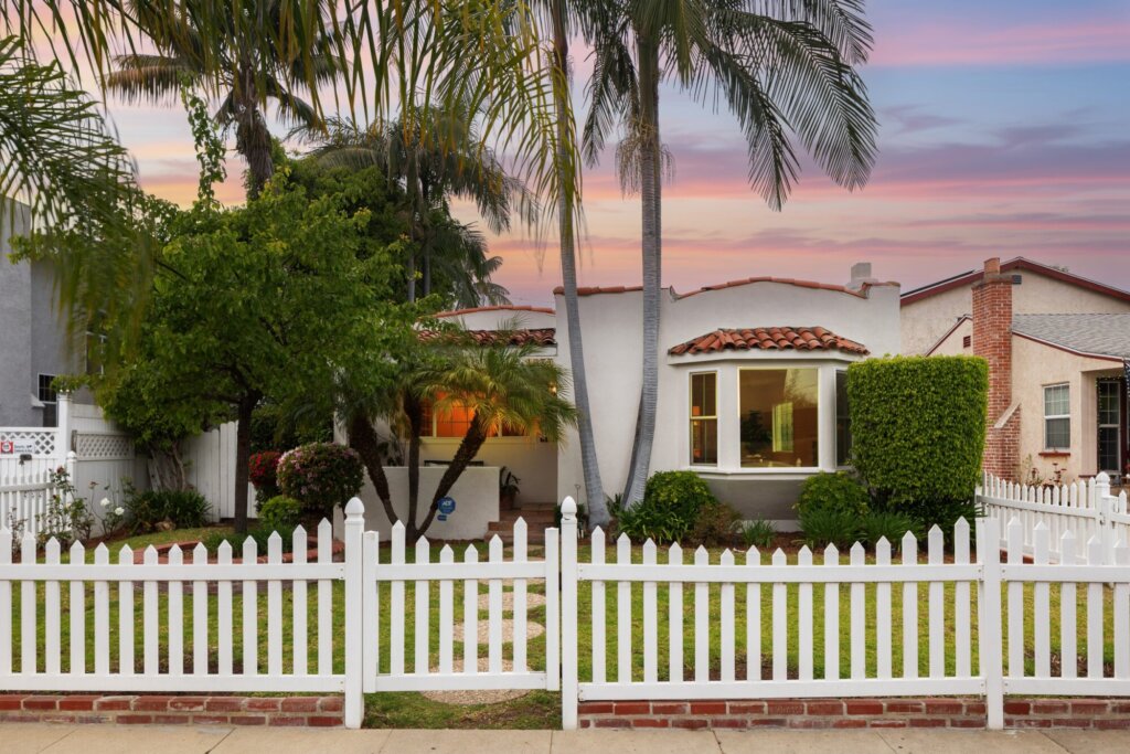 After: the same home at dusk with trimmed hedges, tidy landscaping and a fresh white picket fence