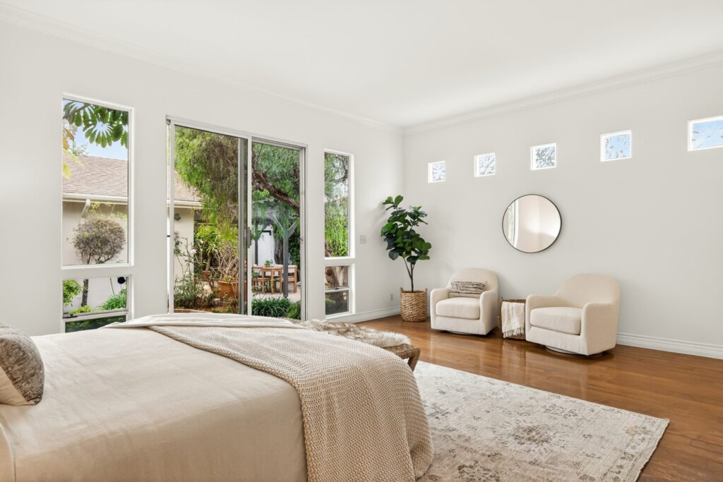 After: the same bedroom painted white and staged with a bed, armchair and plants