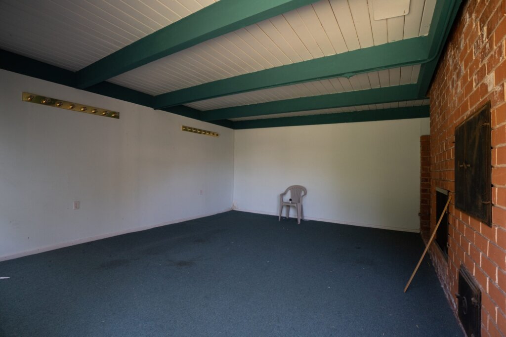 Before: an empty den with green painted ceiling beams and a bare brick fireplace